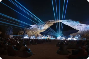 زرقاء Blue and white light beams above an outdoor stage and seated audience