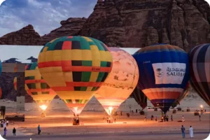 Colourful hot air balloons gathered near buildings beneath sandstone cliffs