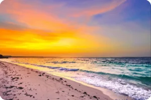 Golden sunset over gentle waves breaking along a sandy beach.