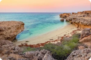 Clear turquoise water washing onto a small sandy beach between rocky outcrops.