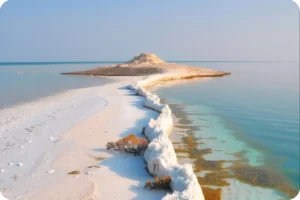 Aerial view of a narrow white sandbar leading towards a small rocky island.