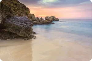 Rocky shoreline beside a sheltered sandy beach at sunset.